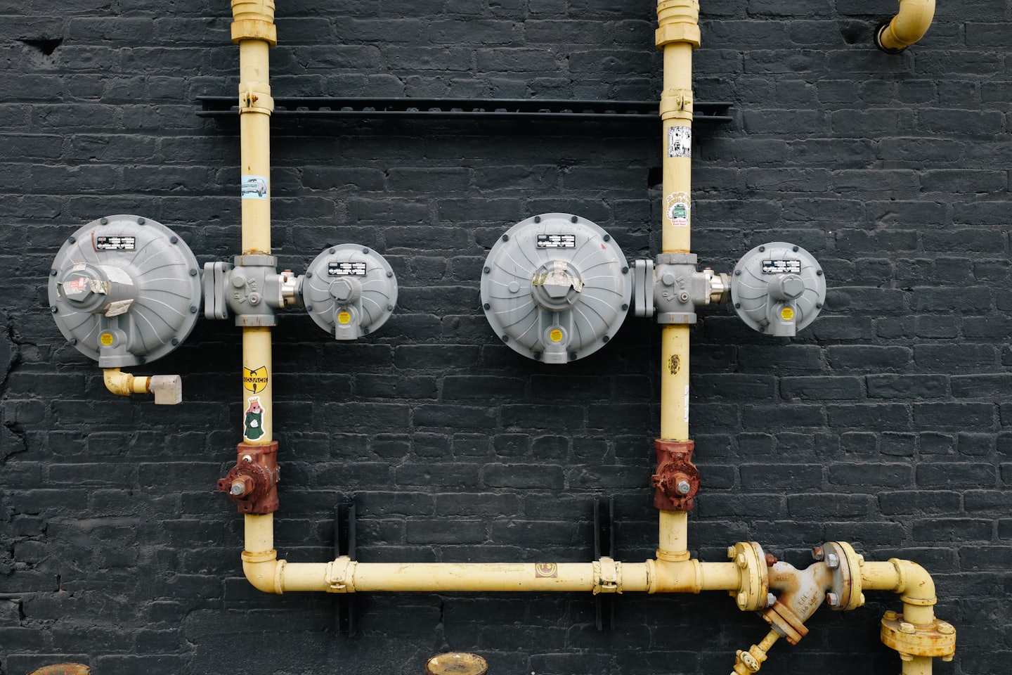 Tubi del gas gialli e contatori montati su un muro di mattoni.