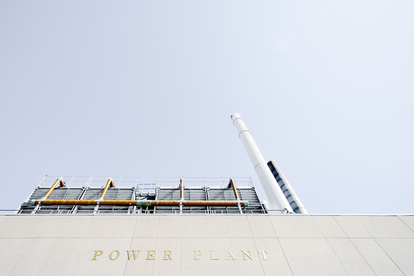 Facciata di una moderna centrale elettrica con scritte dorate e ciminiere bianche.